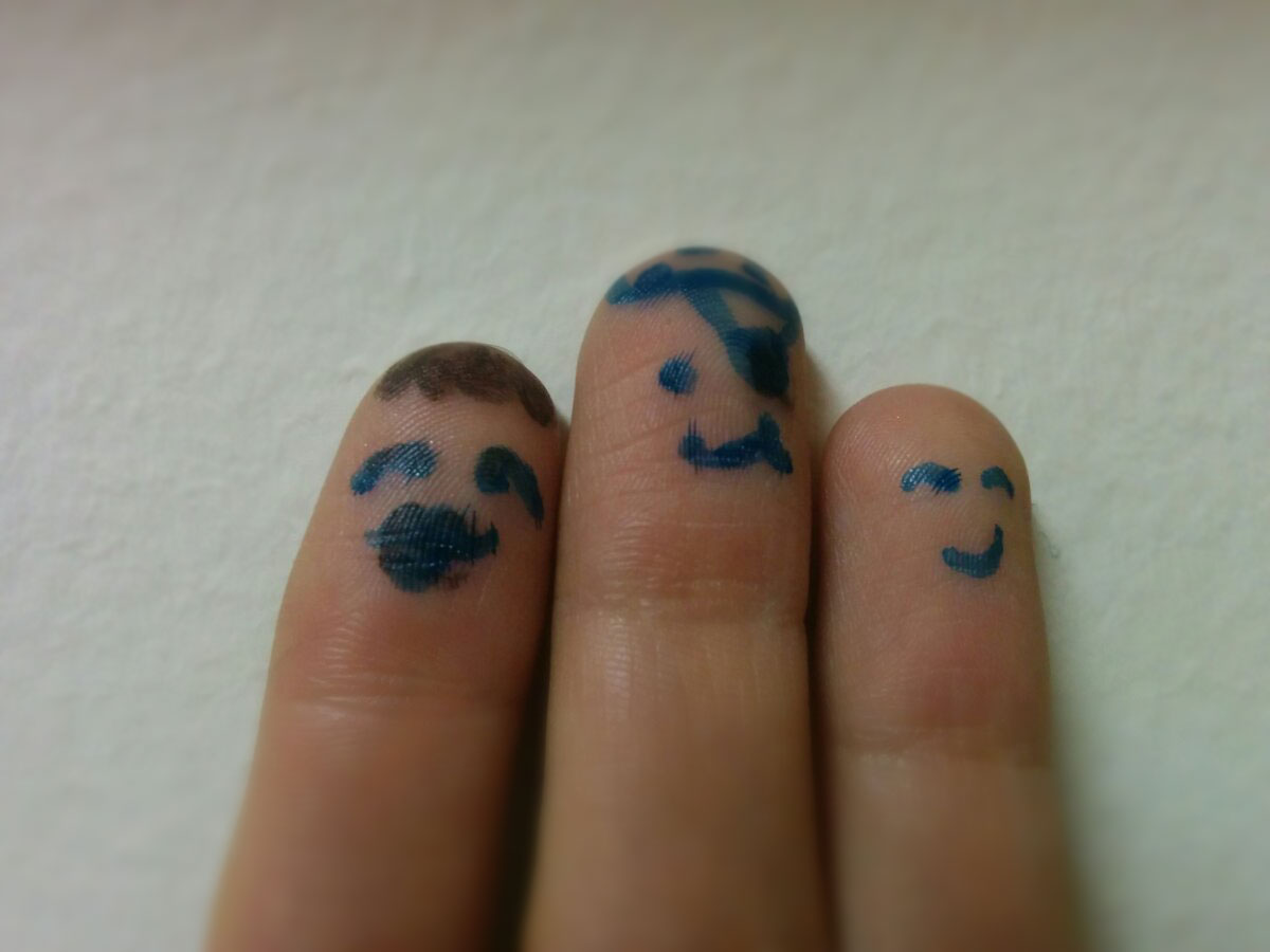 Three fingers with faces drawn on them, stand together.